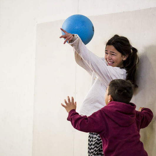 Girl holding blue ball laughing as boy tries to get the ball