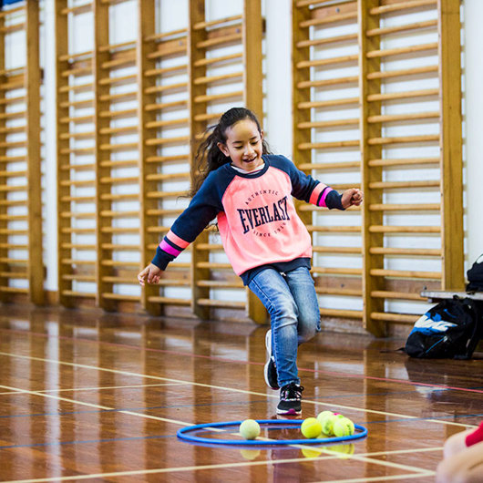 Girl in gym runs towards a hoop and tennis balls on ground