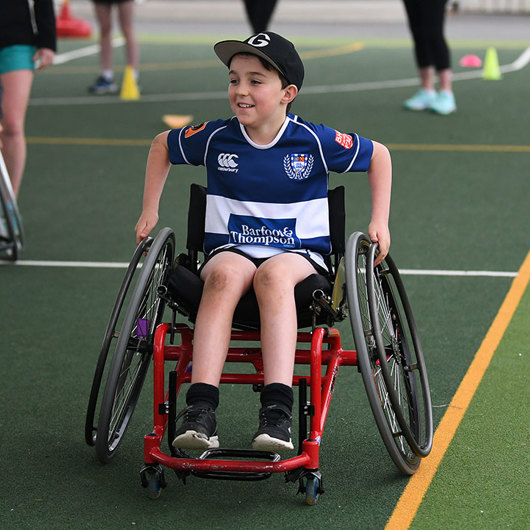 Smiling boy wheels his chair on a sports field