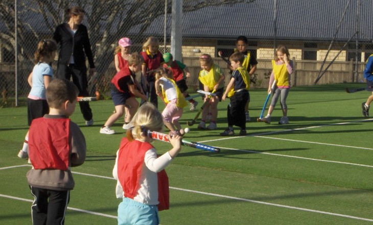 A dozen kids on a turf in teams playing hockey