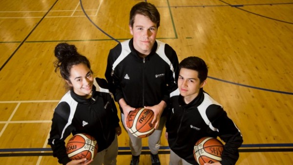 two young men and one young women holding basketballs