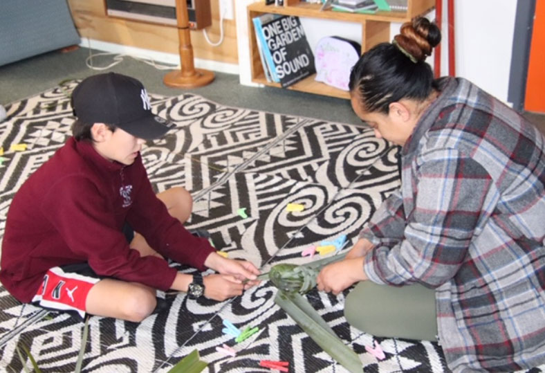 A child and adult doing flax weaving