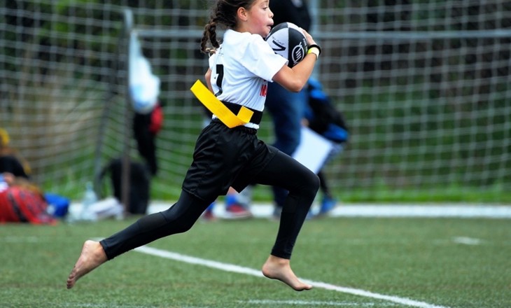 Girl running with rugby ball on field in bare feet