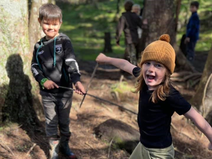 A boy and a girl playing in a forest with sticks