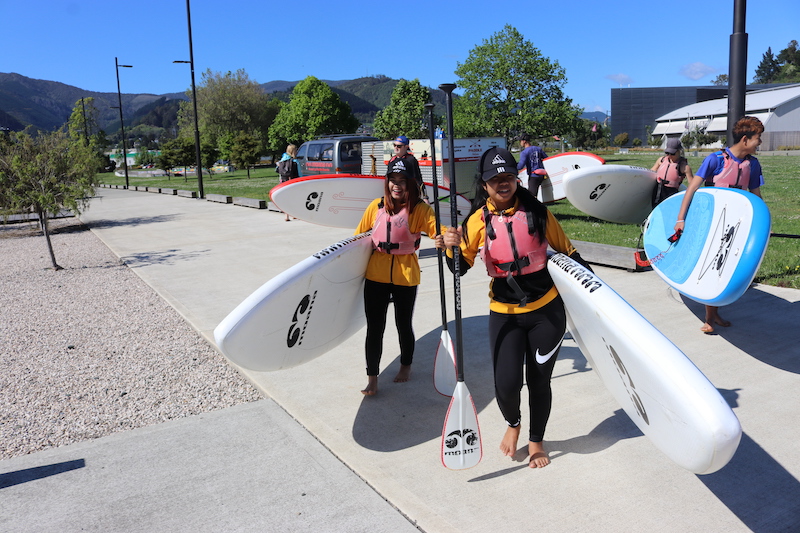 Two young women carrying paddleboards to the beach