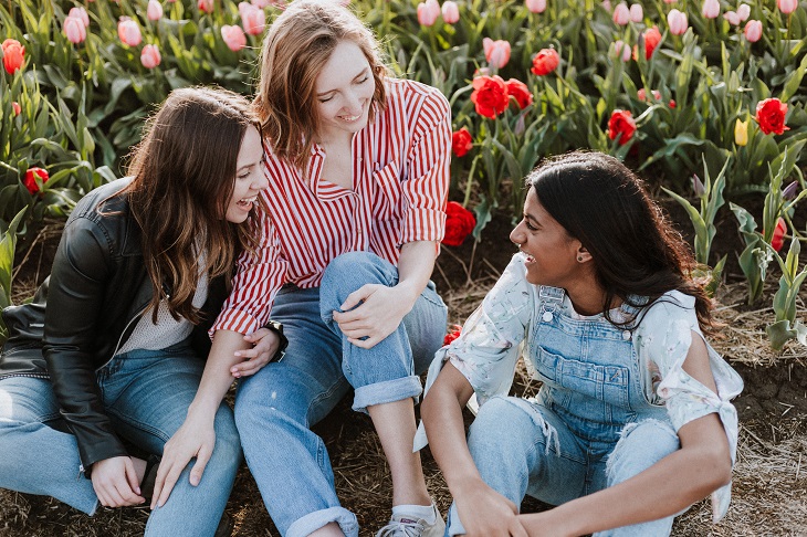 Group of three young women sitting in front of flowers