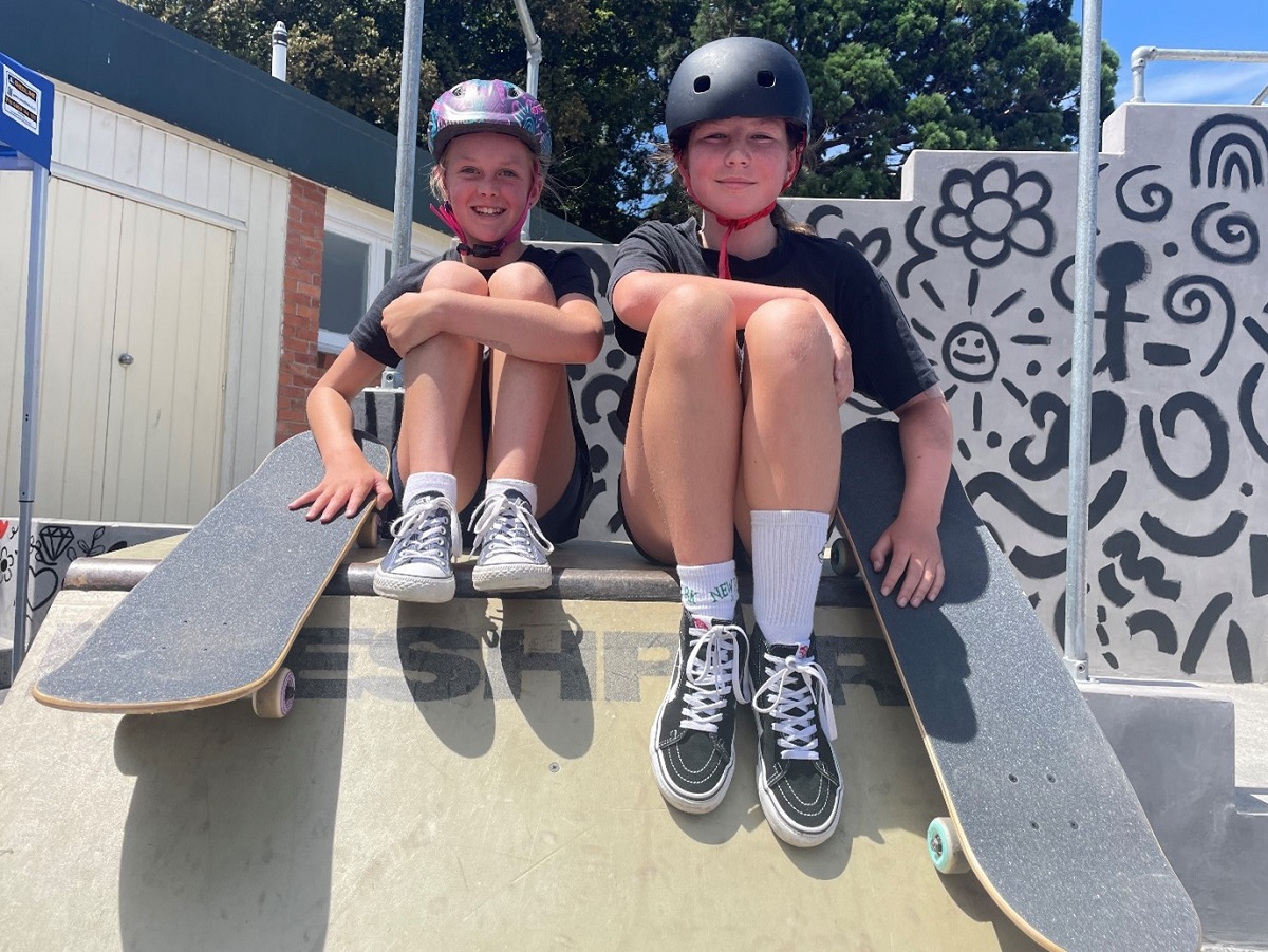 two young women sitting on a ramp with their skateboards