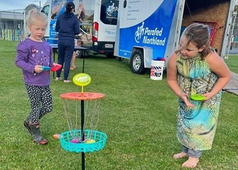 Two tamariki playing with a frisbee goal