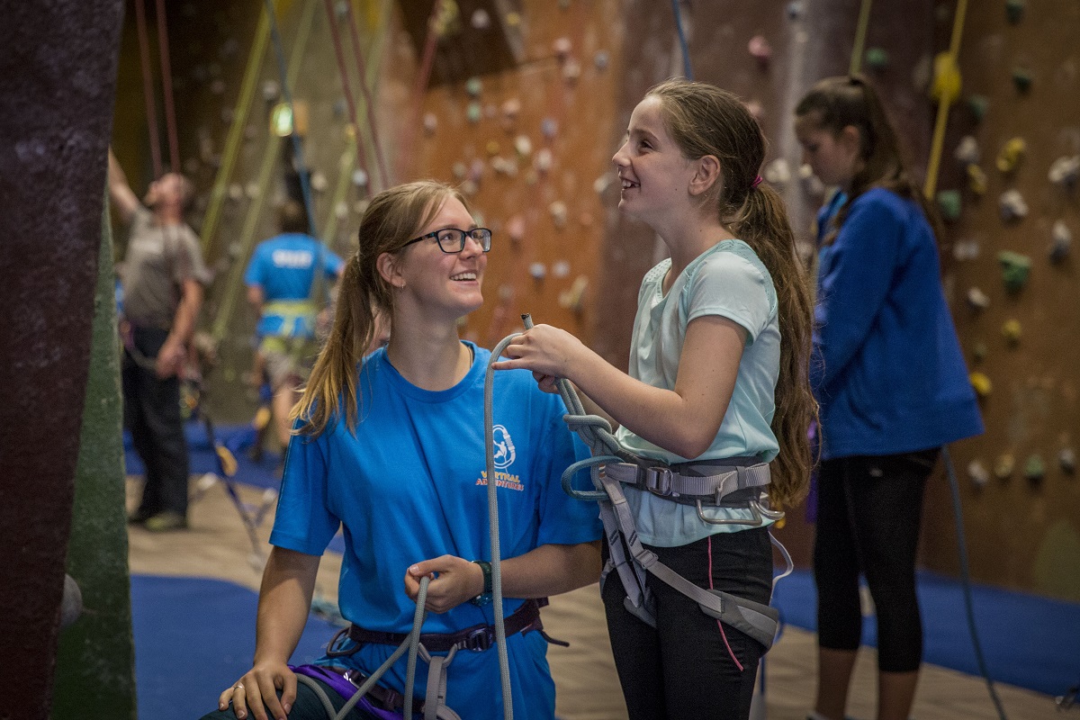 A climbing trainer assisting a child at a climbing gym