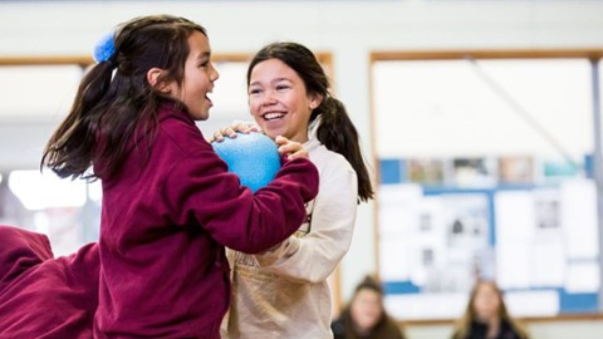 Two girls laughing and fighting over a ball