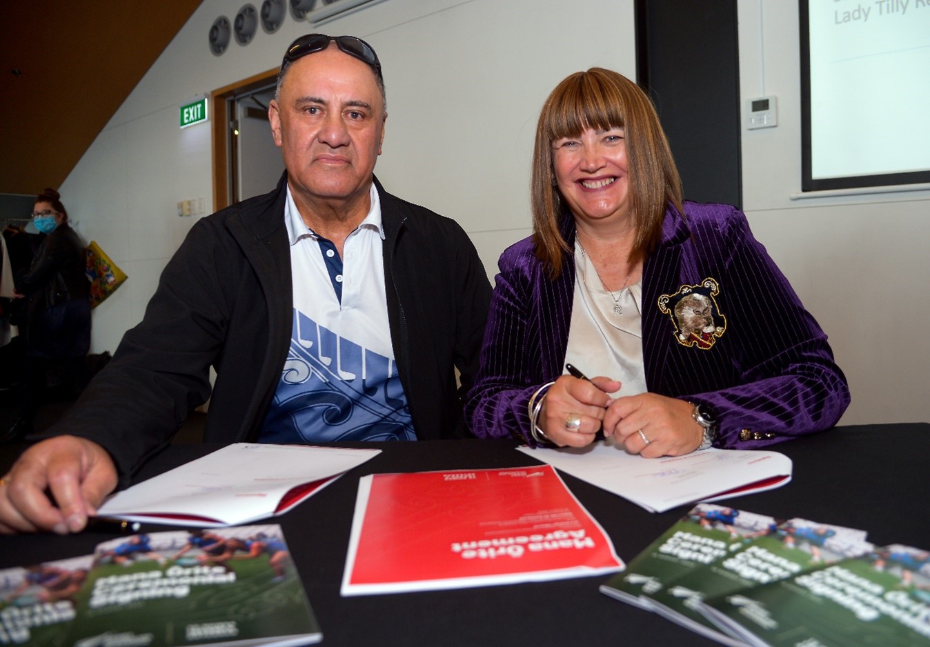 Two people including Raelene Castle sitting at a table signing documents