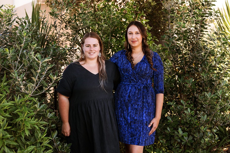 Two women standing in front of trees looking towards the camera