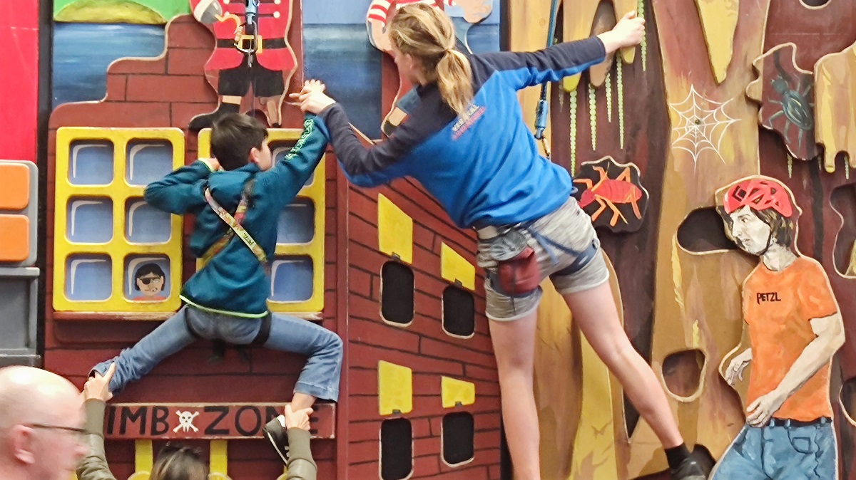 A climbing trainer assisting a child on a climbing wall