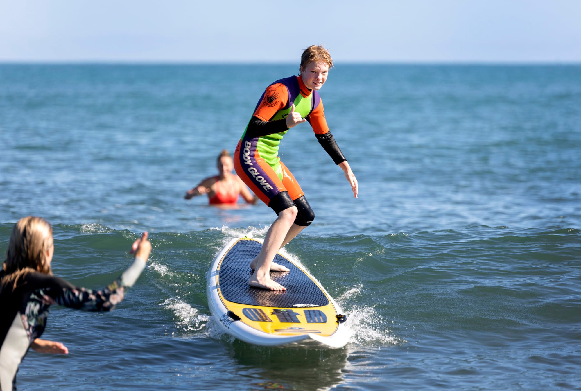 Rangatahi on a surfboard giving the thumbs up to camera